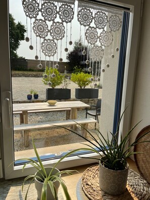 A sliding glass door with a view of an outdoor patio area, including a wooden table and potted plants.