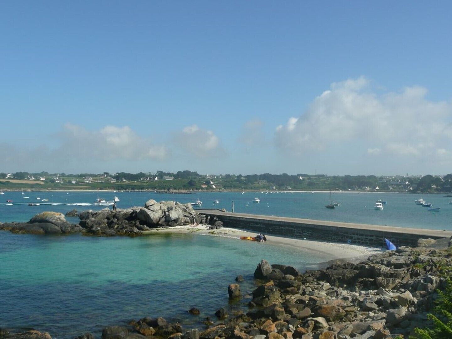 A coastal view with rocky shores, a sandy beach, and boats in the water.
