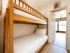 Ein Etagenbett mit Holzrahmen und weißer Bettwäsche, eine Tür zu einem Außenbereich und eine kleine Wanddekoration darüber.