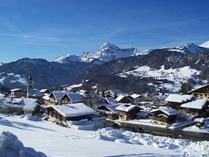 A snow-covered village with traditional wooden houses, a church, and a mountain backdrop.