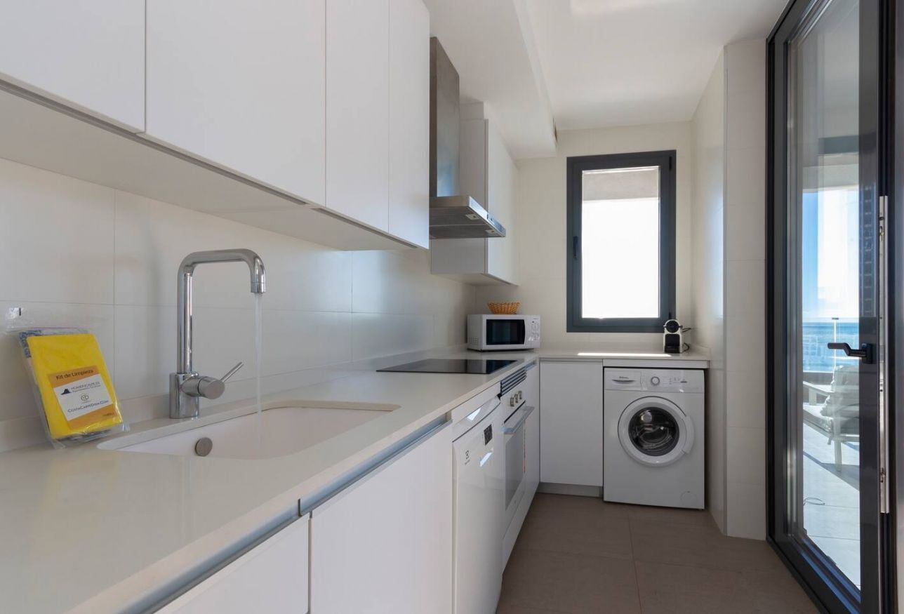 A compact kitchen with white cabinets, a stainless steel sink, a microwave, and a washing machine.