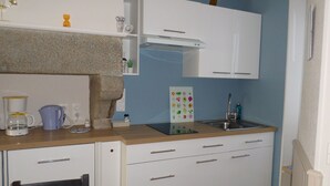 Cozinha compacta com armários brancos, bancada de madeira, cafeteira, pia e uma planta decorativa.