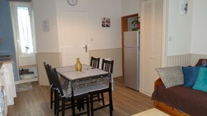 Um espaço de estar compacto com uma mesa de jantar, cadeiras, sofá, frigorífico e um relógio na parede.