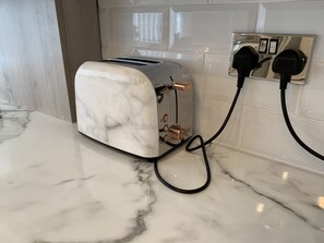 A modern kitchen with a marble countertop, a built-in toaster, and a power outlet with a black cord plugged in. - GuywoodHouse (Stockport)