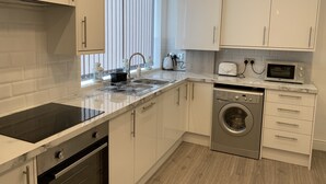 A modern kitchen with white cabinets, a stainless steel dishwasher, a built-in oven, a microwave, and a sink with a dish rack. - GuywoodHouse (Stockport)