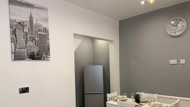 A modern kitchen with a built-in refrigerator, a dining table set for four, and a cityscape poster on the wall. - GuywoodHouse (Stockport)