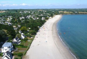 Vue aérienne d’une ville côtière avec une plage de sable, des maisons et une mer bleue et limpide.