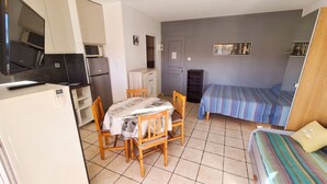 A compact room with a bed, a dining table with chairs, a kitchen area with a microwave and refrigerator, and a television.