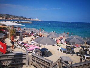 Ein Strand mit vielen Sonnenschirmen und Liegestühlen, freier Blick auf das Meer und eine Stadt in der Ferne auf dem Hügel.
