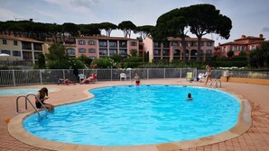A swimming pool with a tiled deck, surrounded by a white fence and a row of buildings in the background.