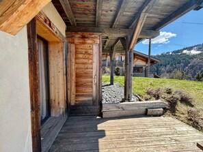 Fachada de madera con un porche cubierto que da a una casa, rodeada de césped y montañas al fondo.