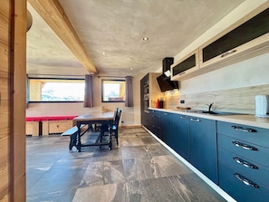 Une cuisine moderne avec des meubles de couleur sombre, une table à manger en bois et une grande fenêtre.