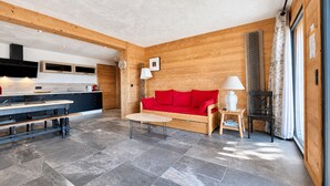 A modern interior with a kitchen, dining area, and living space featuring a red sofa, wooden walls, and stone flooring. - Charming apartment with large terrace and parking (Notre-Dame-de-Bellecombe)