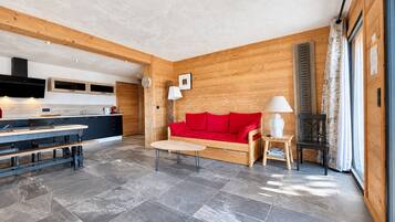 Een modern interieur met keuken, eethoek en zithoek, met een rode bank, houten wanden en stenen vloer.