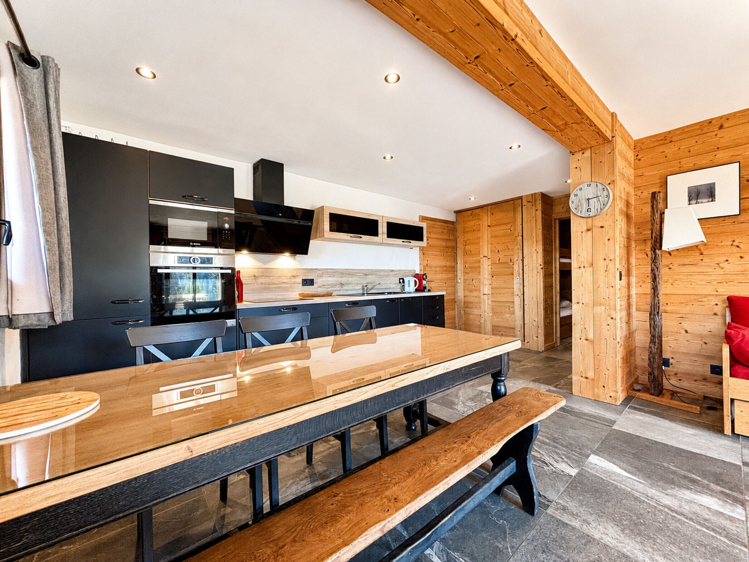 Een moderne keuken met een lange houten tafel, geïntegreerde apparatuur en een houten plafond.