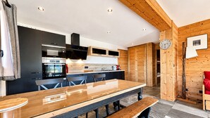 A modern kitchen with a long wooden table, built-in appliances, and a wooden ceiling. - Charming apartment with large terrace and parking (Notre-Dame-de-Bellecombe)