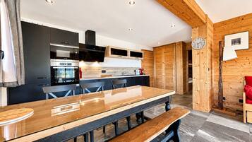 Een moderne keuken met een lange houten tafel, geïntegreerde apparatuur en een houten plafond.