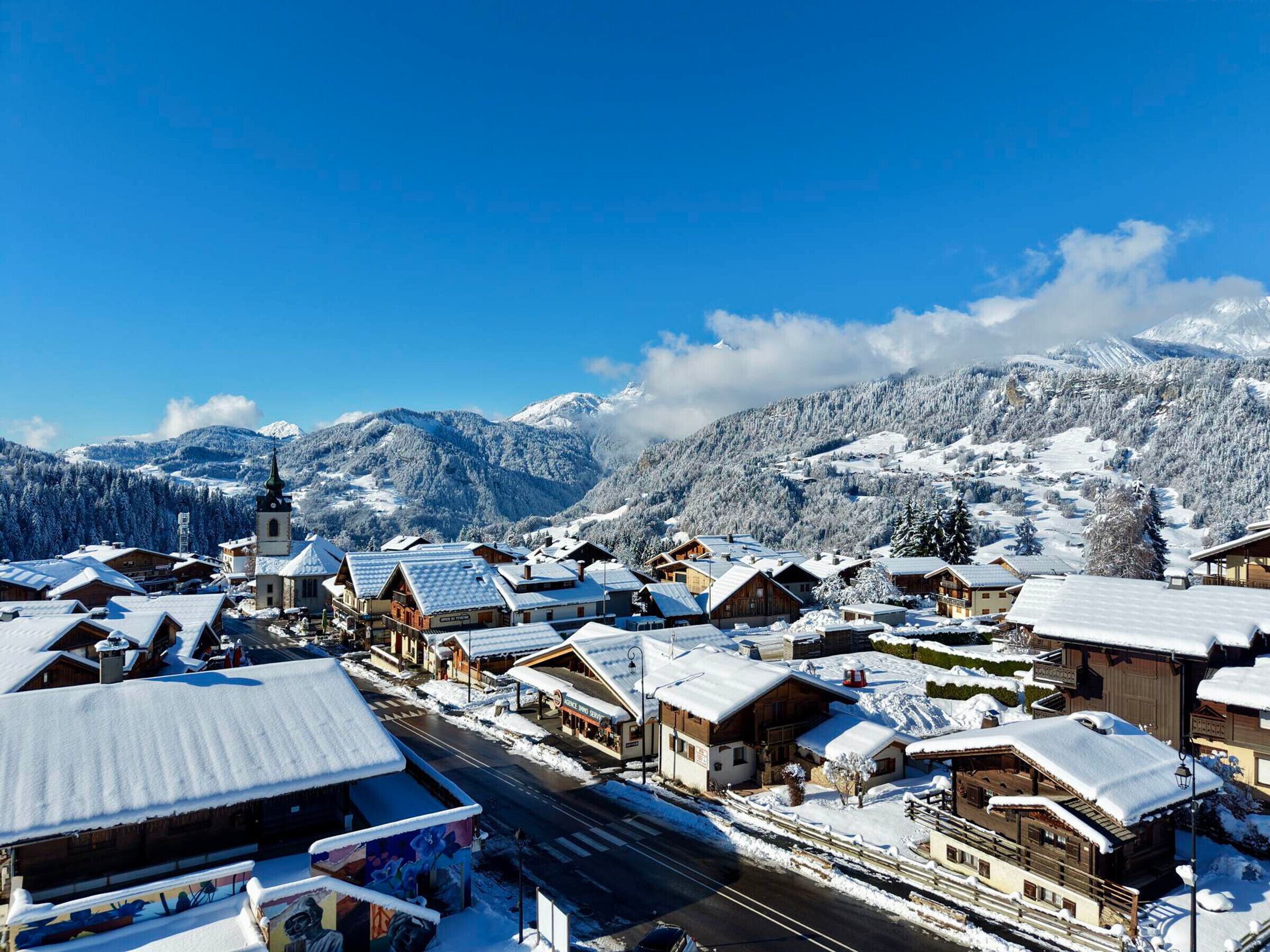 A snow-covered village with wooden buildings, a church, and mountains in the background.