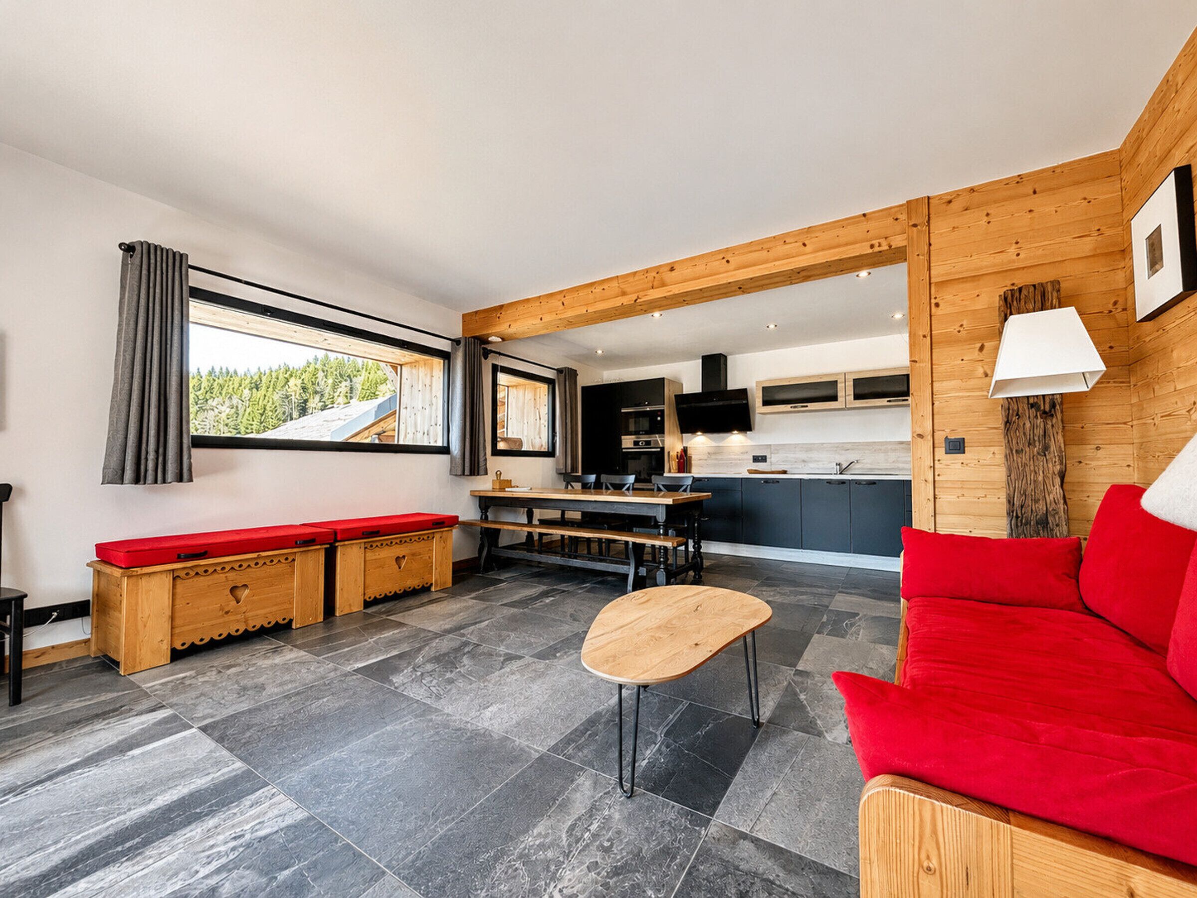 Een modern interieur met een houten bank, een rode bank, een kleine tafel, en een keuken met kastjes en een televisie.
