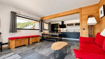 Een modern interieur met een houten bank, een rode bank, een kleine tafel, en een keuken met kastjes en een televisie.
