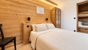 A bedroom with a wooden headboard, a bed with a beige bedspread, a nightstand with a lamp, and a wardrobe with a glass door. - Charming apartment with large terrace and parking (Notre-Dame-de-Bellecombe)