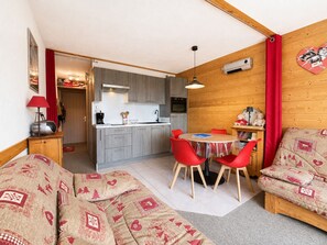 Un espace de vie compact comprenant un coin cuisine, un coin repas avec des chaises rouges et un canapé recouvert d’un tissu à motifs.
