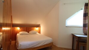 A small, cozy bedroom with a single bed, wooden headboard, and a window with a view.