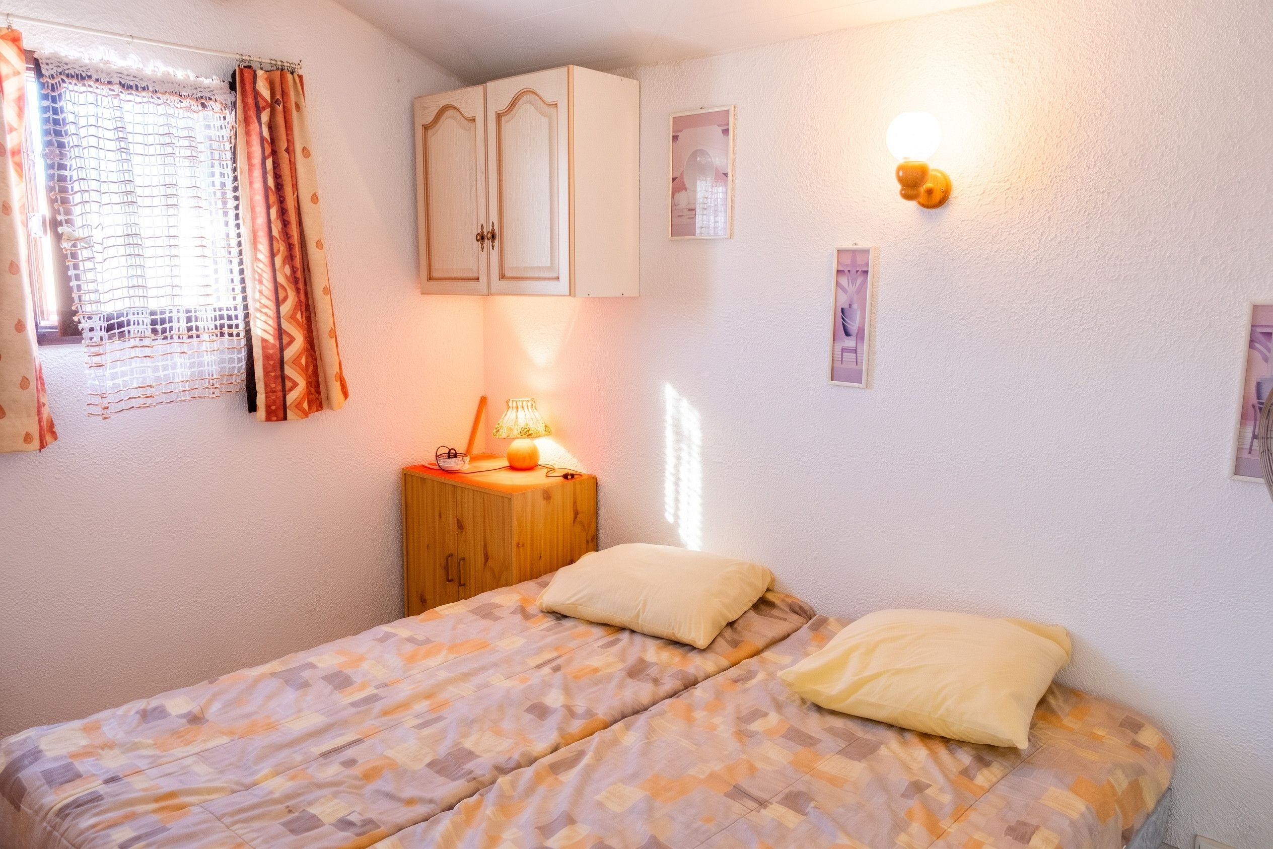 Une chambre à coucher avec un lit, une table de chevet, une lampe et une fenêtre avec des rideaux.