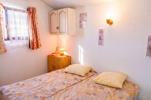 Une chambre à coucher avec un lit, une table de chevet, une lampe et une fenêtre avec des rideaux.