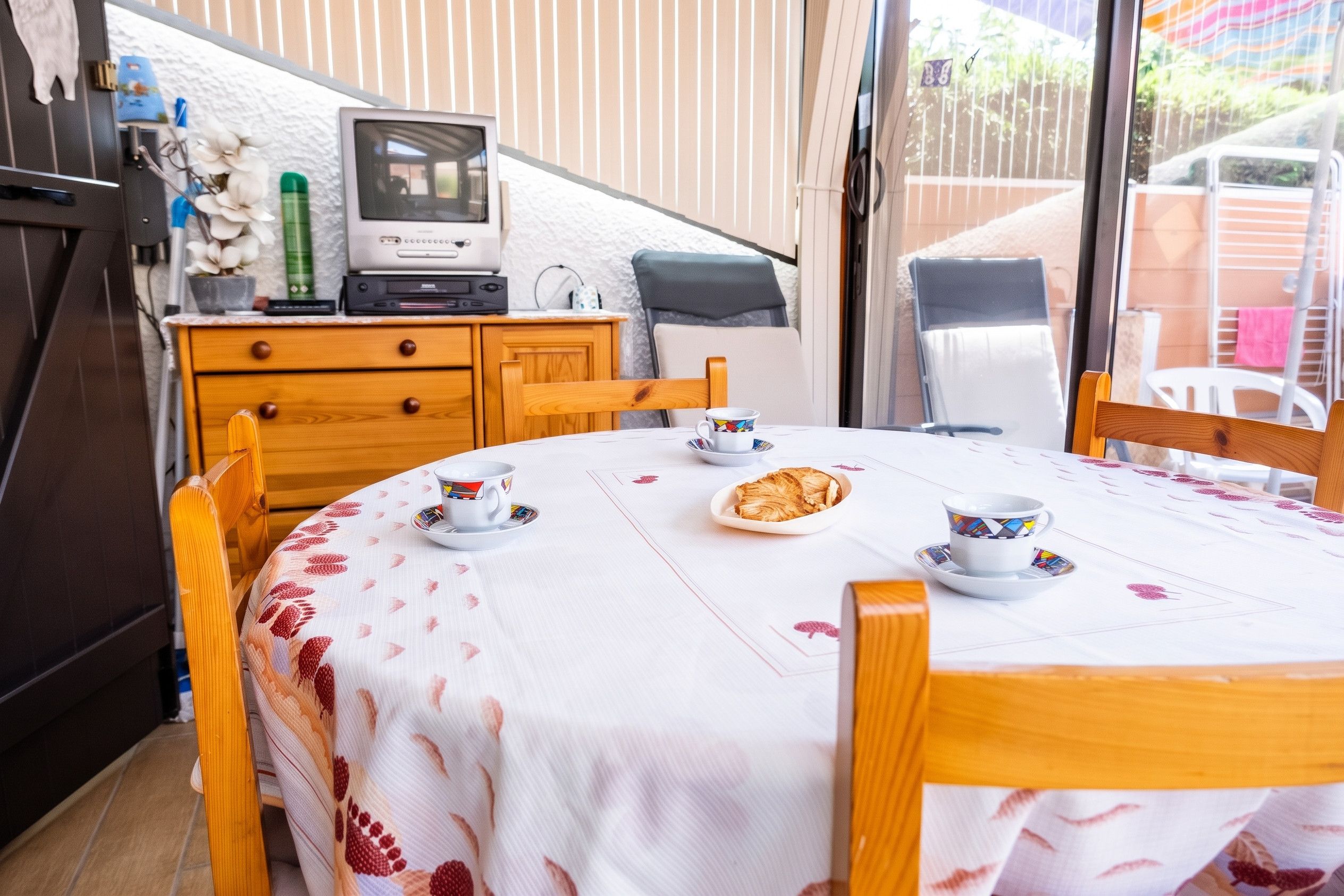 A compact kitchen with a dining table set for two, a television, and a small cabinet.