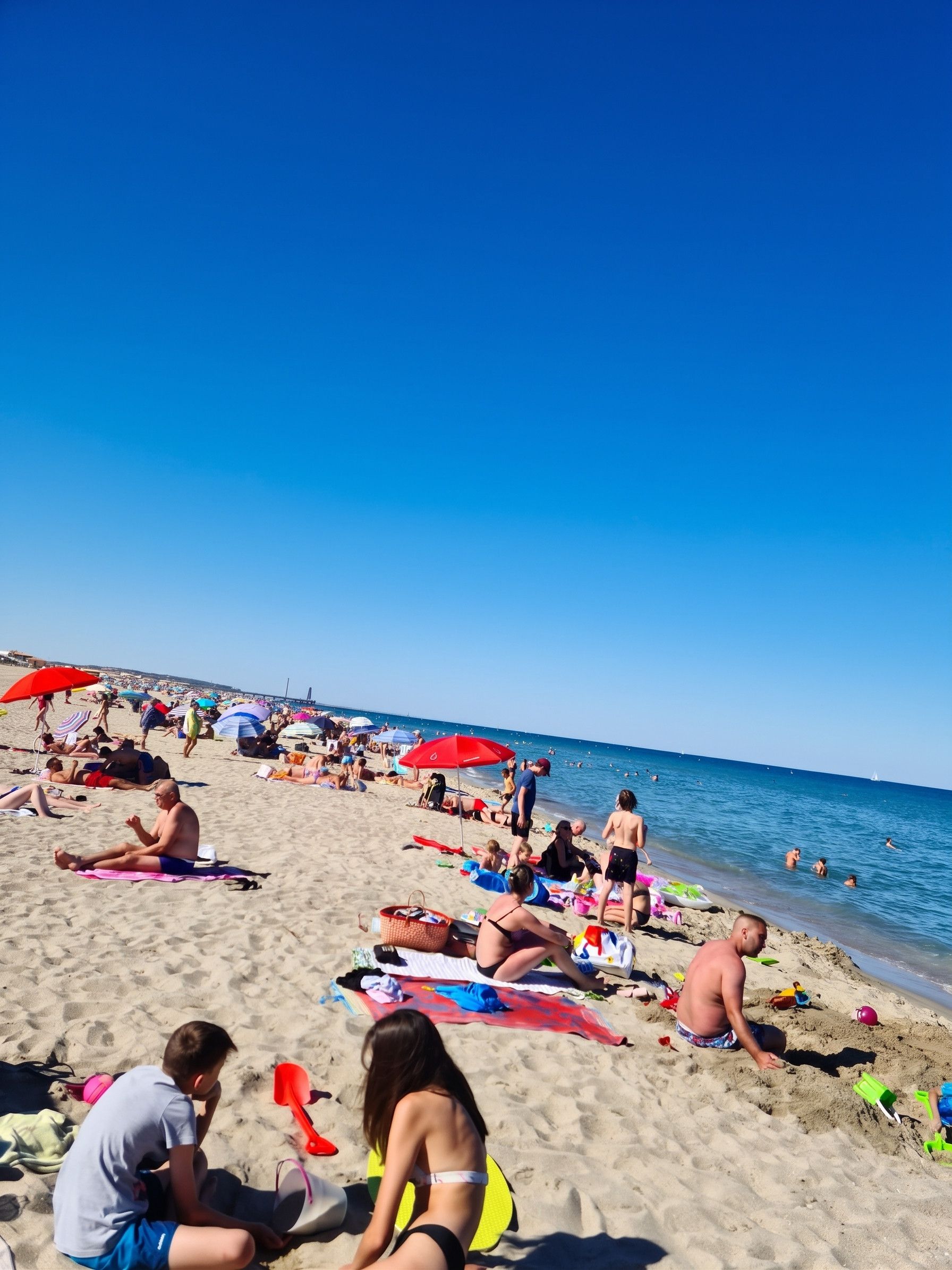 A crowded beach with people sunbathing and swimming.