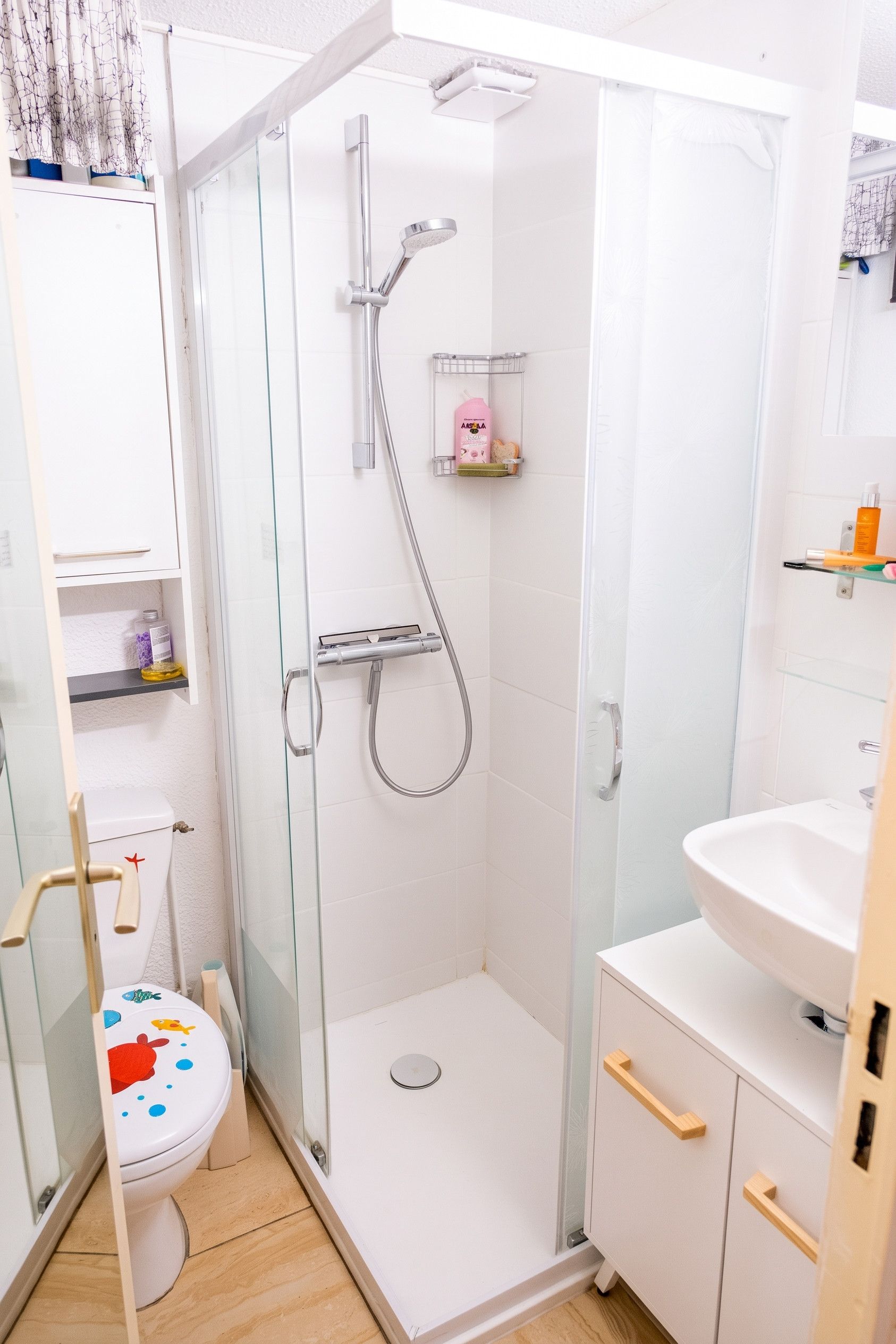 Ein modernes Badezimmer mit einer Duschkabine aus Glas, einer weißen Toilette mit farbigem Dekor und einem Waschbecken mit Spiegel.