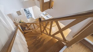 Un escalier en bois avec une rampe métallique, menant à une pièce dotée d’un plancher en bois et d’un mur blanc.