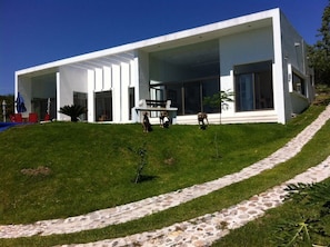 Una casa moderna con un amplio porche abierto, un camino de piedra y un césped.