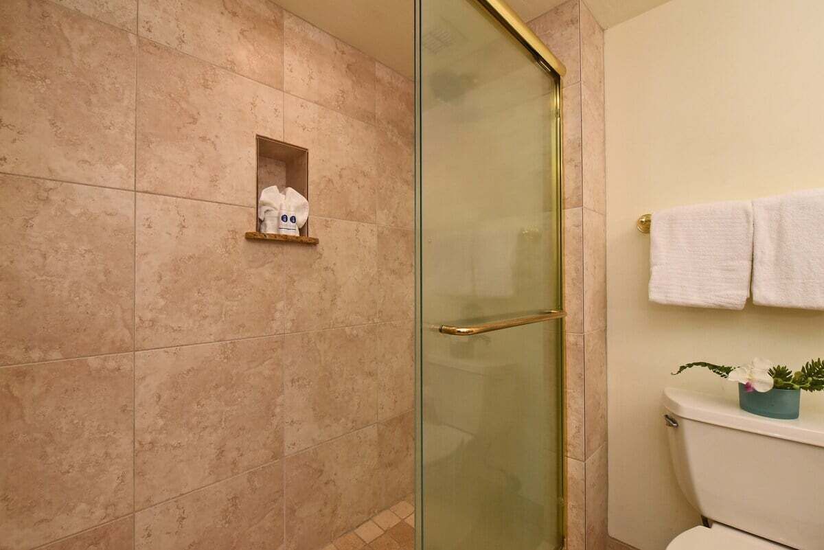 Une salle de bain avec une porte de douche en verre, des toilettes ornées d’un pot de fleurs bleu et une étagère sur laquelle est posée une serviette blanche.