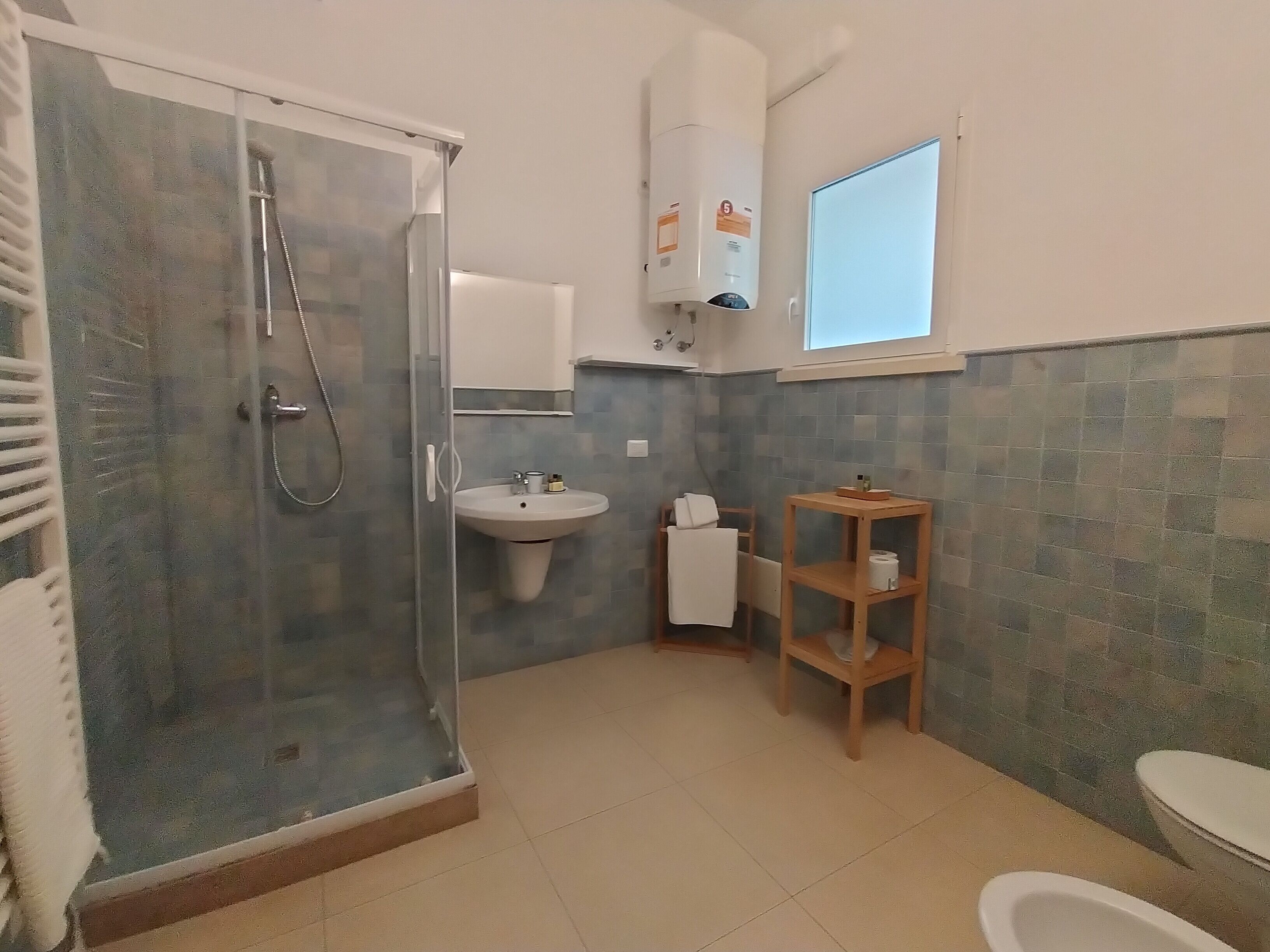 A bathroom with a glass shower enclosure, a sink, a wooden shelf, and a toilet.