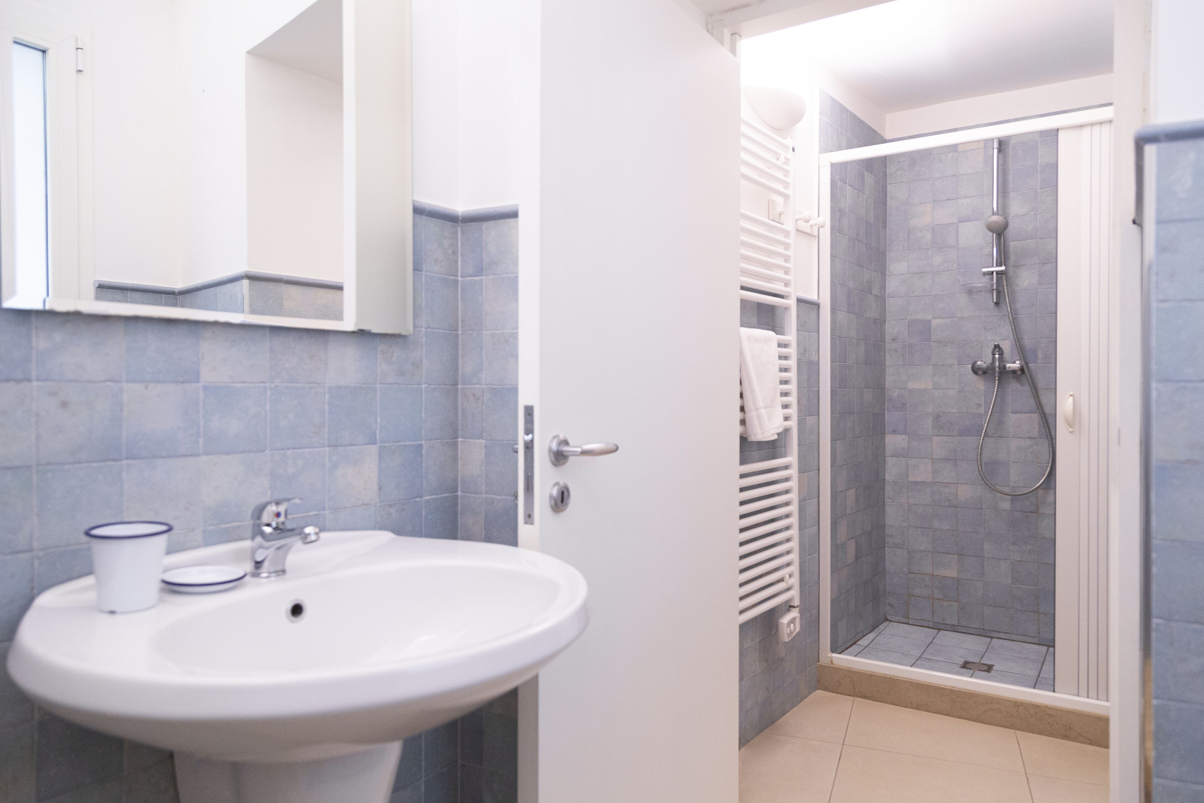 Une salle de bain avec un lavabo blanc, un miroir et un espace douche doté d’une porte en verre.