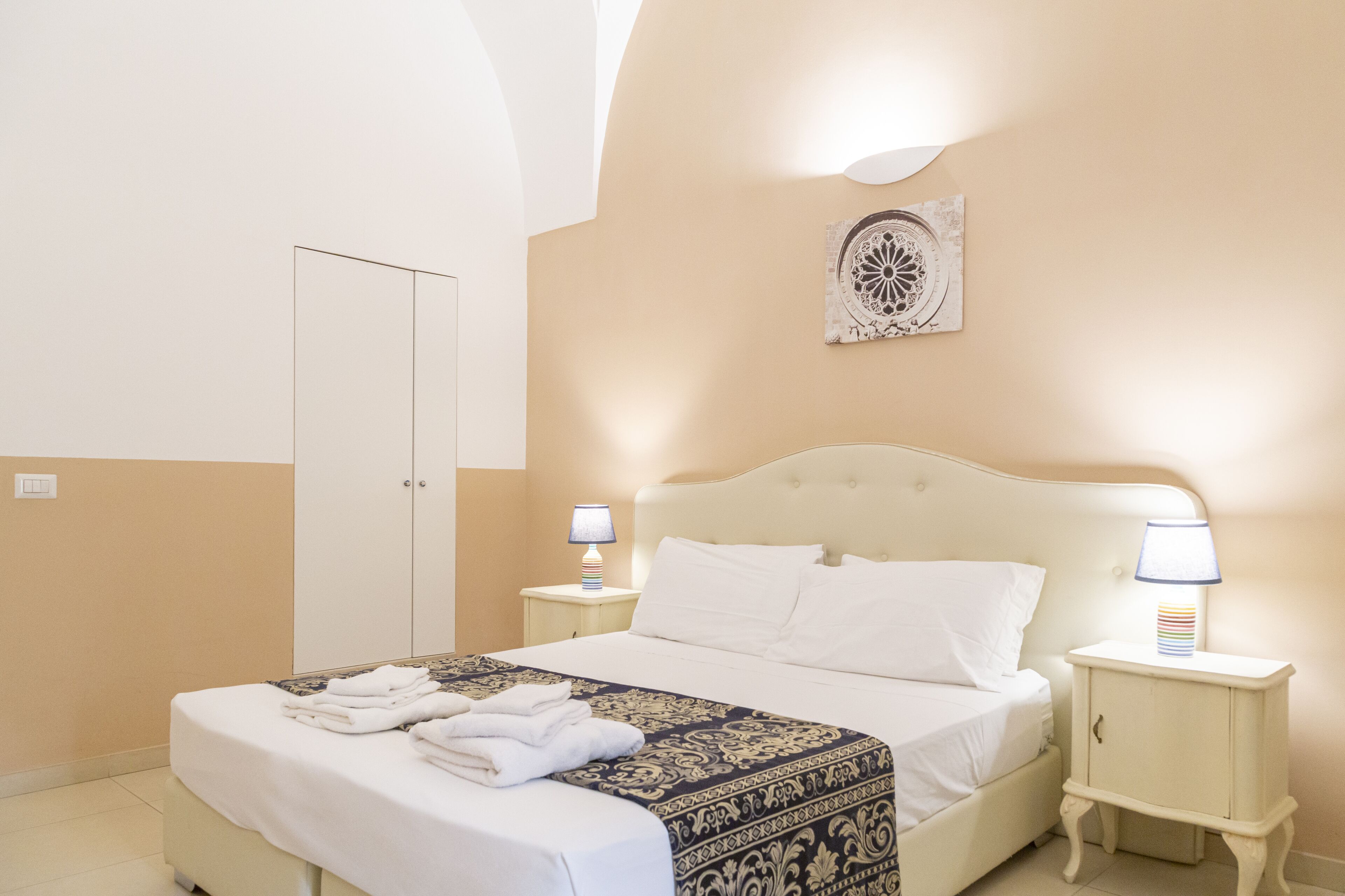 Una cama bien hecha con un edredón estampado, dos lámparas de noche y un mueble pequeño.