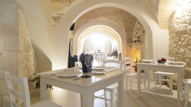A dining area with white furniture, stone walls, and a view through an arched doorway. - Casa Mamma Elvira (Lecce)