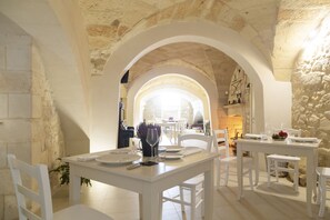 A dining area with white furniture, stone walls, and a view through an arched doorway. - Casa Mamma Elvira (Lecce)