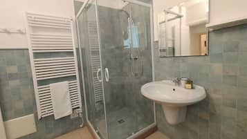 Un bagno con doccia vetrata, lavandino bianco e portasciuga.