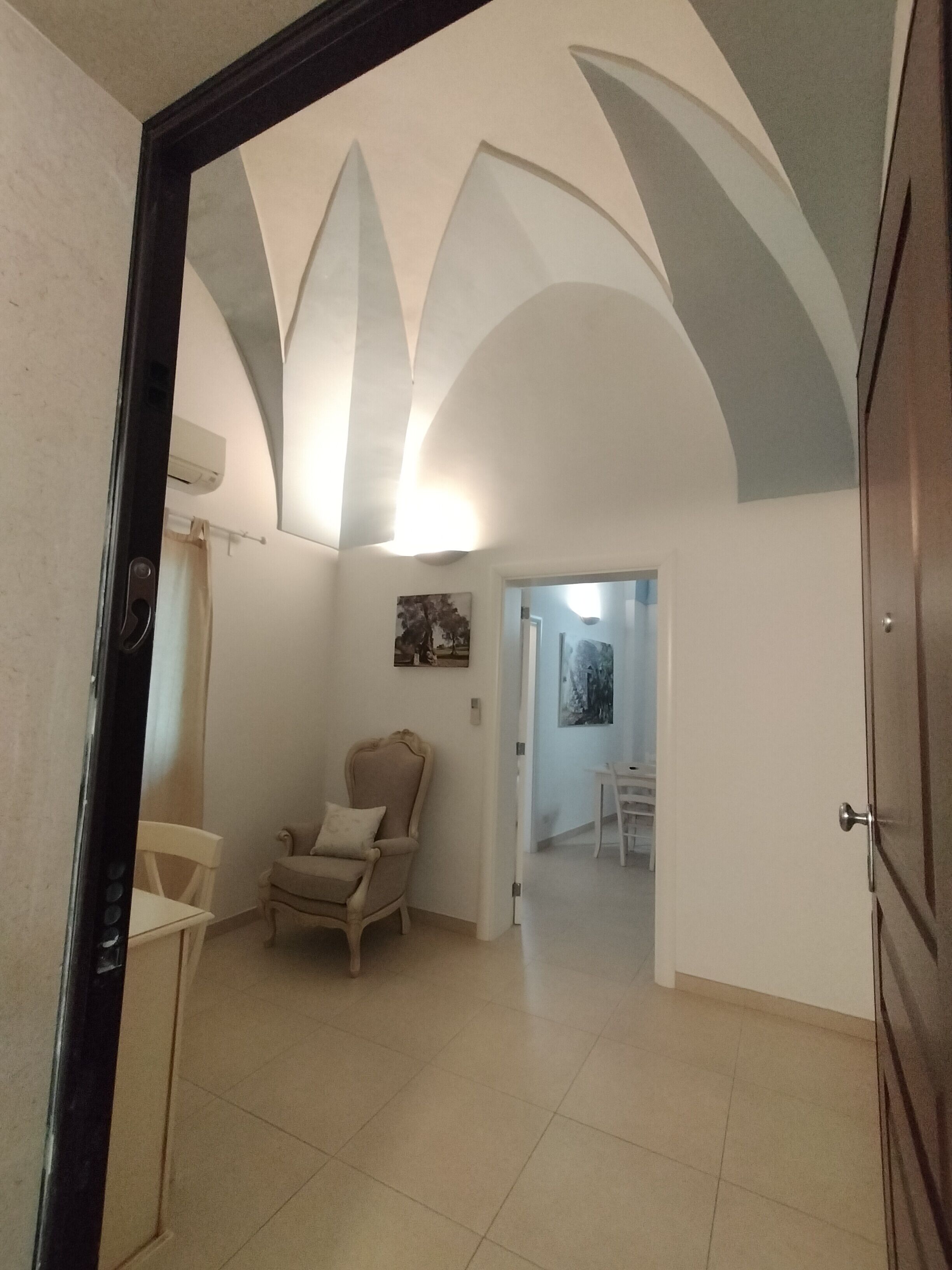 A spacious room with a high ceiling, a wooden door, a beige armchair, and a white chair.