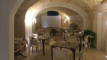 An indoor dining area with stone arches, tables, chairs, and a large white screen.