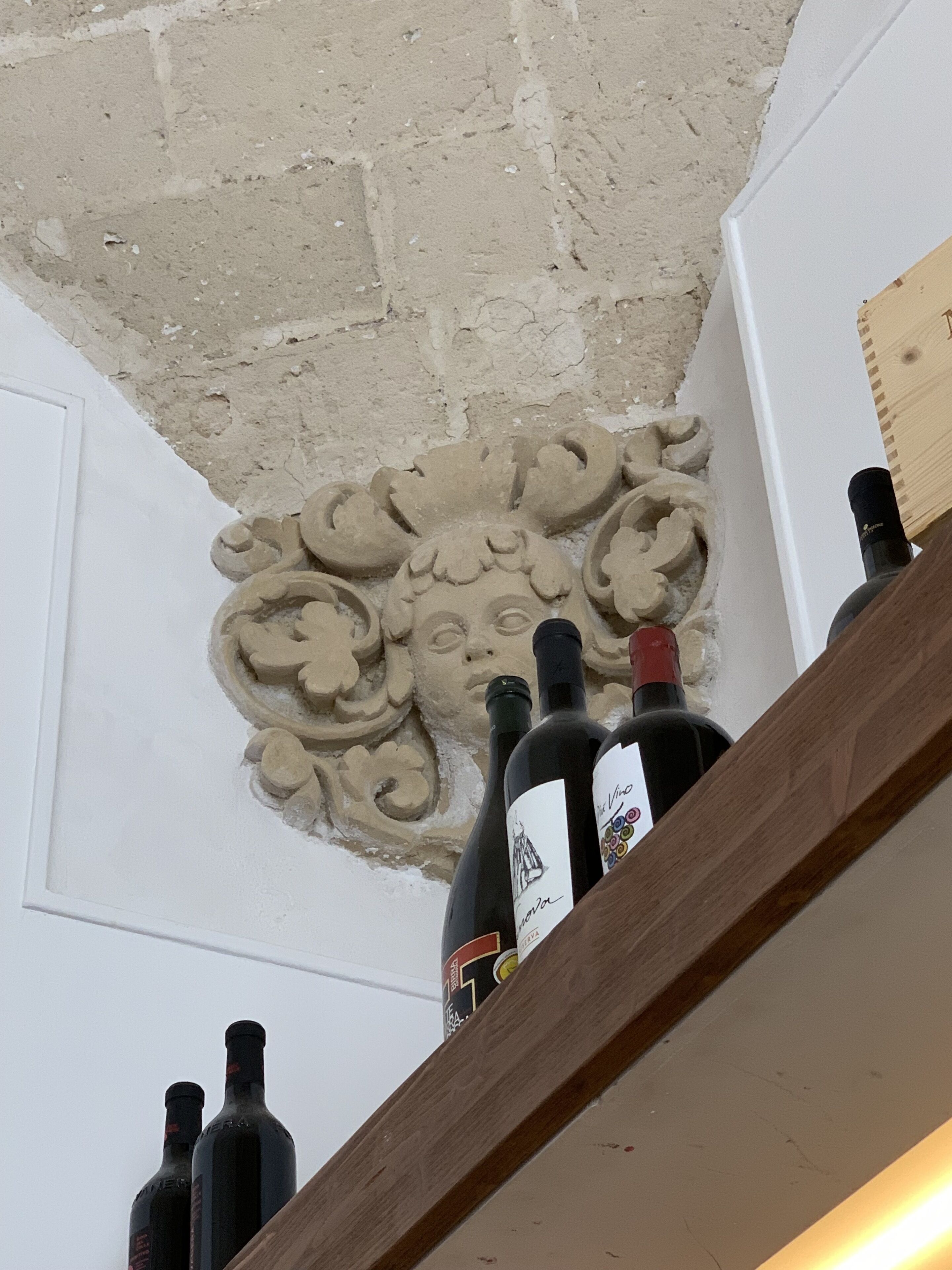 A wine rack with bottles, a decorative plaster ceiling, and a wooden beam.
