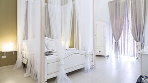 A four-poster bed with white bedding and sheer curtains, a bedside table, and a nightstand. - Casa Mamma Elvira (Lecce)