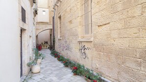A narrow stone-paved alley with potted plants and a building with a window and graffiti. - Casa Mamma Elvira (Lecce)