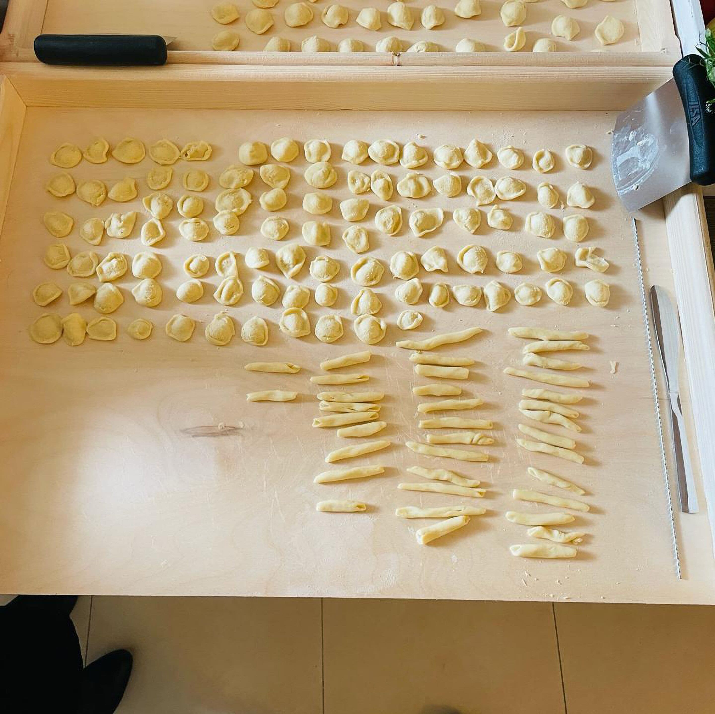 A wooden cutting board with various pasta shapes and a knife.