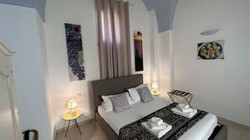 Une chambre d’hôtel comprenant un lit, deux tables de chevet, une commode, une fenêtre avec des rideaux et des œuvres d’art mural.