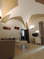 Una sala de estar con un sofá, una mesa de centro, un televisor sobre un mueble bajo y una puerta que da a otra habitación.