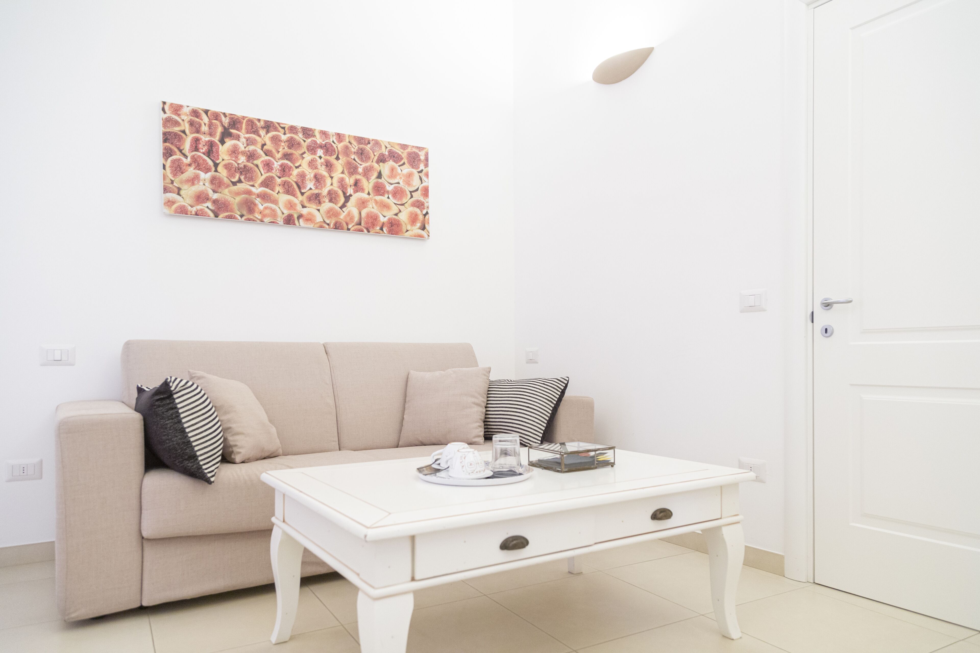 A minimalist living room with a beige sofa, a white coffee table, and a wall-mounted abstract art piece.